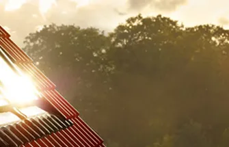 Velux dakraam met zonlicht op een dak met groene bomen in de achtergrond en Velux-logo rechtsboven