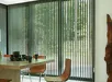 Tafel met stoelen voorvenster met groene lamelgordijnen en houten sculptuur
