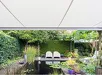 Gesloten semi-cassette zonwering boven een tuin met waterpartij en bankjes