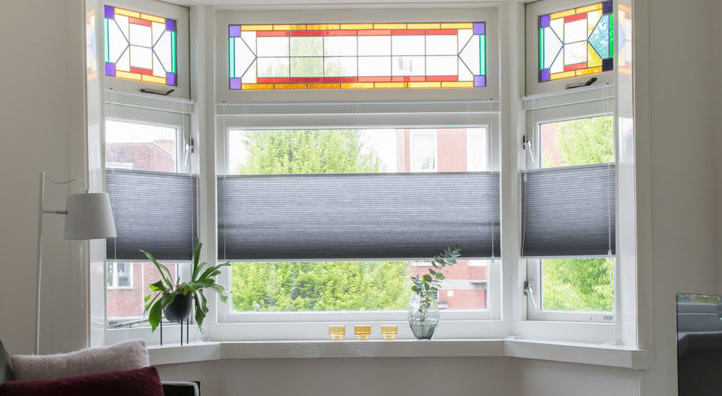 Grijze top-down plissegordijnen voorzien van kleurrijke glas-in-lood bovenlichten in een woonkamer