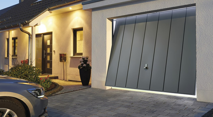 Grijze Hormann garagedeur geïnstalleerd aan een huis met verlichting en auto in de buurt