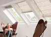 Vrouw in witte trui zit op stoel met Velux vouwgordijn FH-B