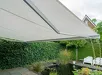 Knikarmzonwering in halfopen stand boven tuin met groen hek