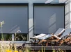 Gesloten Alulux rolgordijn voor twee ramen met buitenruimte en ligstoelen