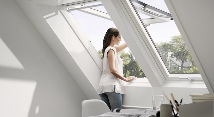 Vrouw die een open Velux dakraam in een woonkamer opent, met uitzicht op buitengebied