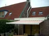 Grijs knikarmscherm gemonteerd onder een pannendak met tuinmeubels