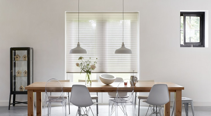 Eetkamer met plisse gordijnen, houten tafel, grijze stoelen en twee hanglampen boven het raam
