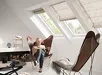 Vrouw in witte trui zit op stoel met Velux vouwgordijn FH-B