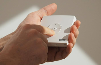 Hand houdt wit Velux bedieningspaneel met draaiknop en logo