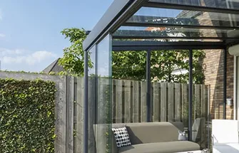 Moderne terrasoverkapping met zitbank en groene privacyheg in een tuin