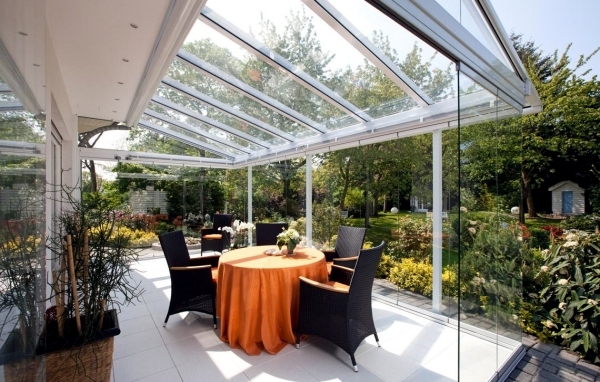 Glas terrasoverkapping met tafel en stoelen in tuin met groen en bloemen