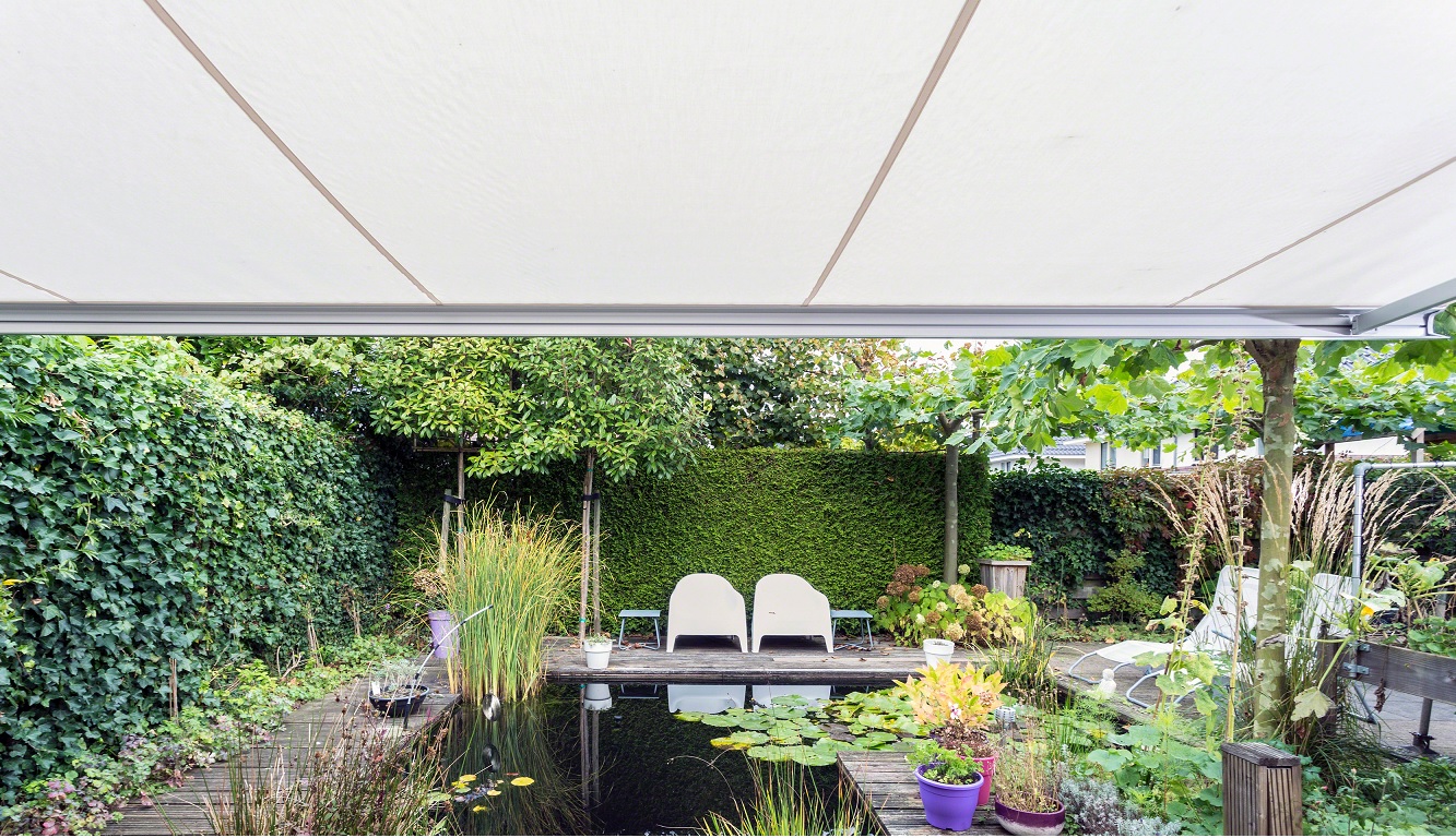 Zonwering uitvalscherm boven tuin met zitbank, planten en waterpartij