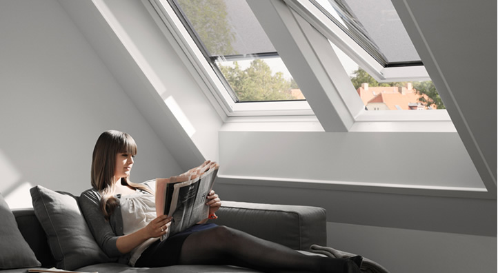 Vrouw die op bank zit en krant leest onder Velux dakramen met zonwering