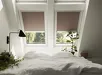 Bed met wit beddengoed en twee dakramen met bruin verduisterend rolgordijn, planten op nachtkastjes