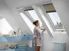 Vrouw in bloemenjurk bedient VELUX jaloezie bij raam